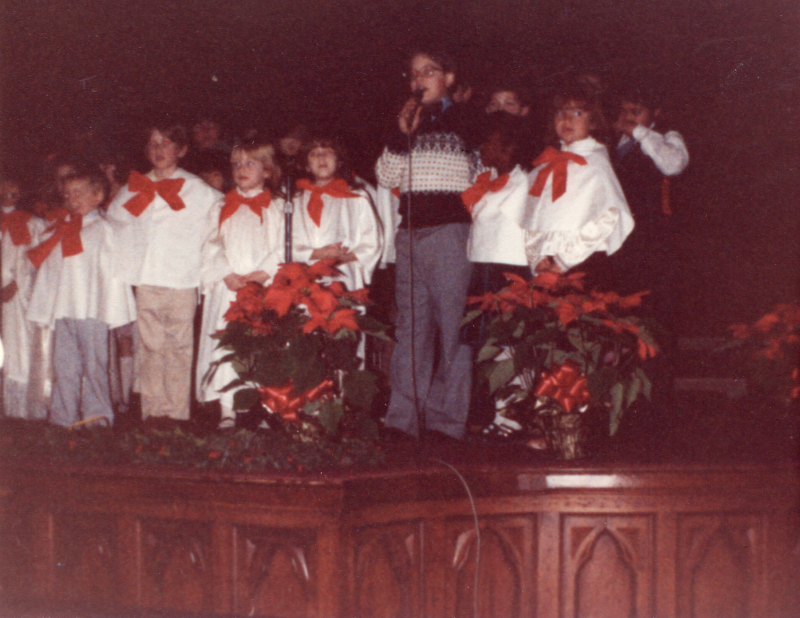 Children in holiday-themed outfits perform together on stage in the sanctuary