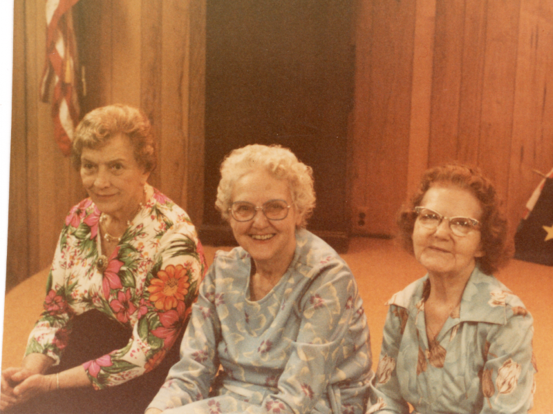 Three older women smile together for a photograph