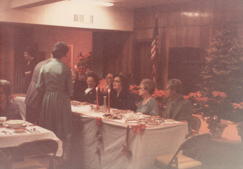 Members of the congregation dine together with a Christmas tree and pointsettias in the backgroun
