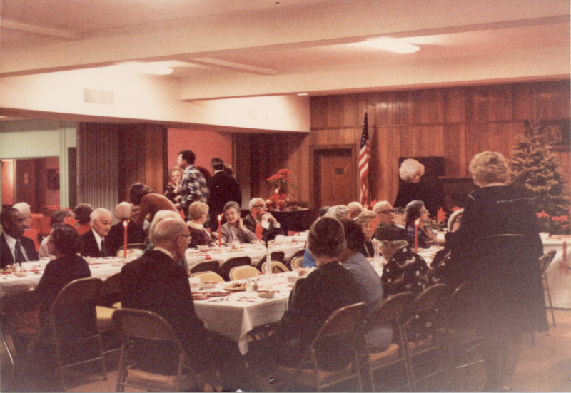 Congregants dine together with a Christmas tree and pointsettias in the background