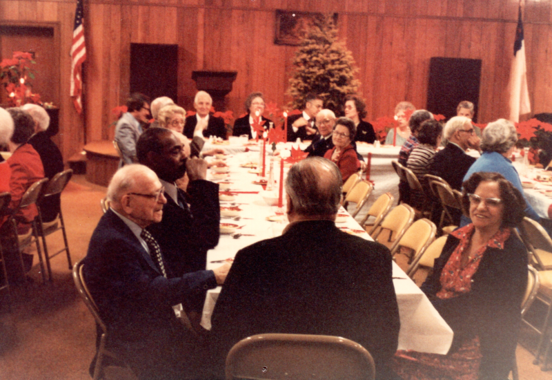 Congregants dine together with a Christmas tree and pointsettias in the background