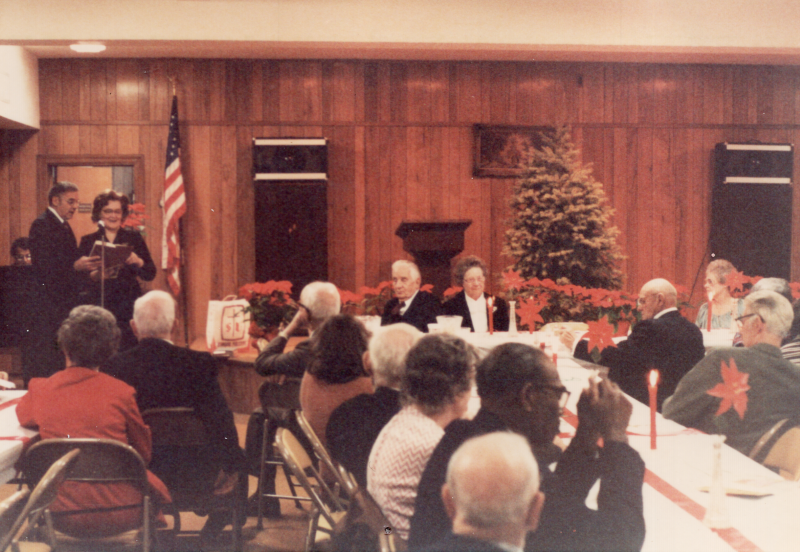 Pastor and Mrs. Bogdan lead congregants in a hymn surrounded by Christmas decorations and with a piano accompanist