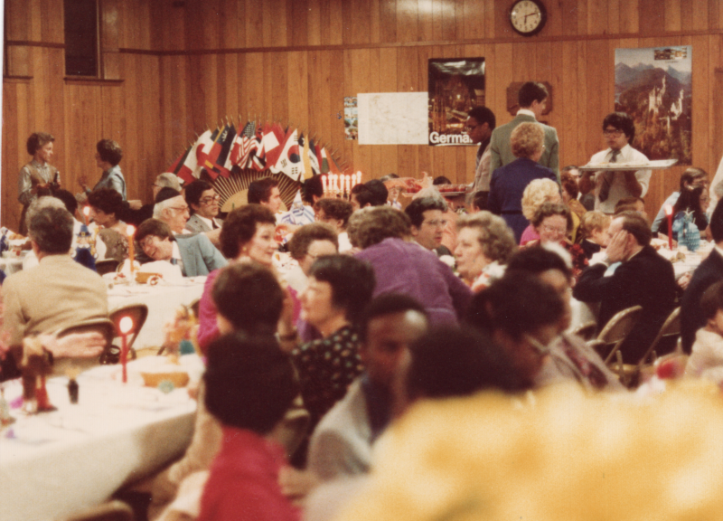 People  dine together around tables. World flags are in the background