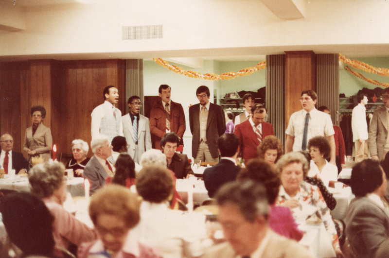 A group of men sing to a group of congregants dining together