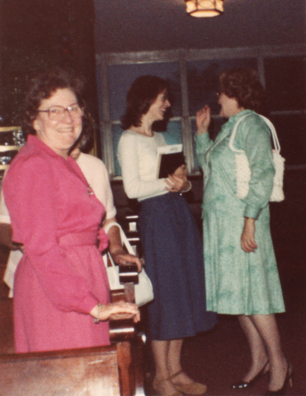 Two women speak in the background as another woman smiles for a photograph