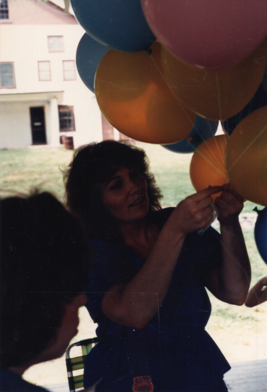 A woman ties together blue, pink, and yellow balloons