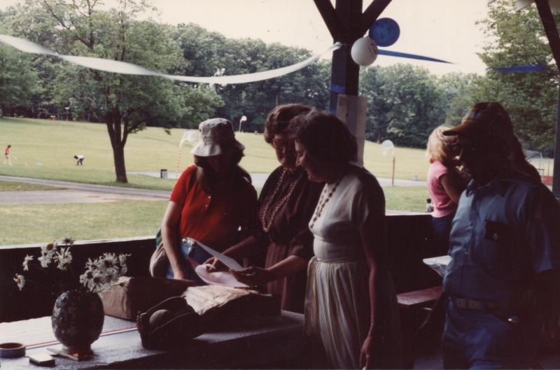 Women look at a piece of paper at a picnic table with blue and white decorations in the background