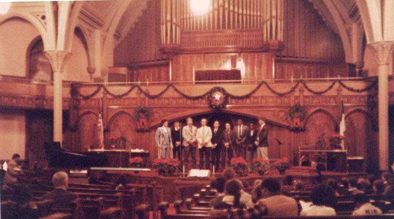 A group of men sing together in the sanctuary with a piano accompanist