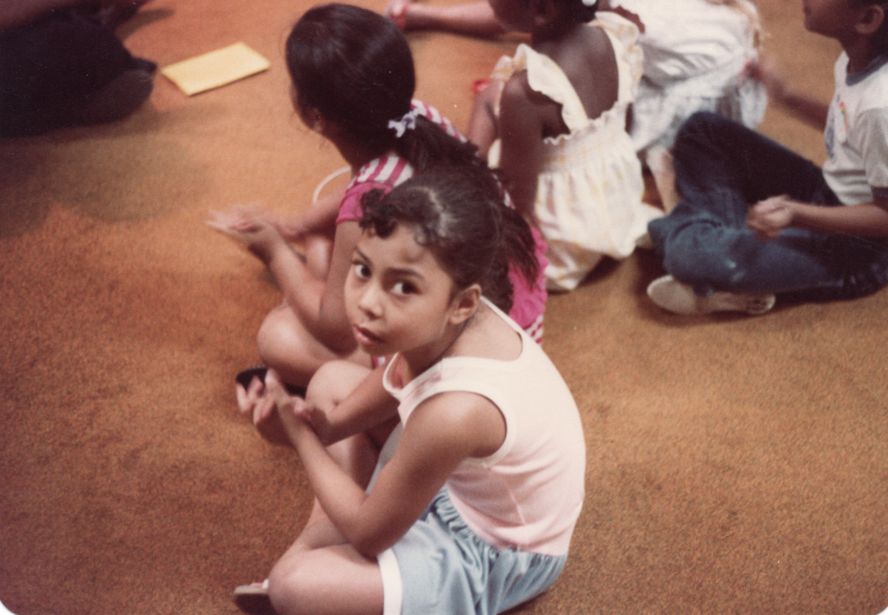Children sit around a woman who is leading them in an activity