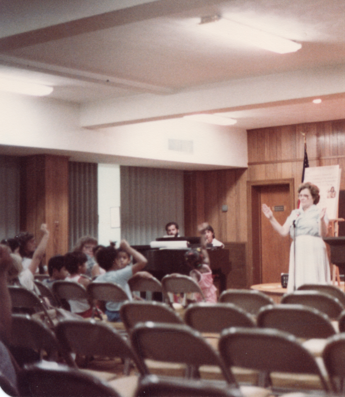 Mrs. Bogdan and a pianist lead a group of children in a song with hand motions