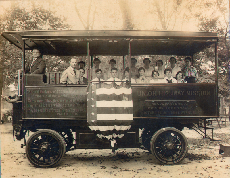 Pastor E.S. Williams smiles with other congregants in the Gospel Wagon that is decorated with Isaiah 1:18, an American flag, and the church's name and address