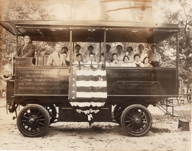Pastor E.S. Williams smiles with other congregants in the Gospel Wagon that is decorated with Isaiah 1:18, an American flag, and the church's name and address