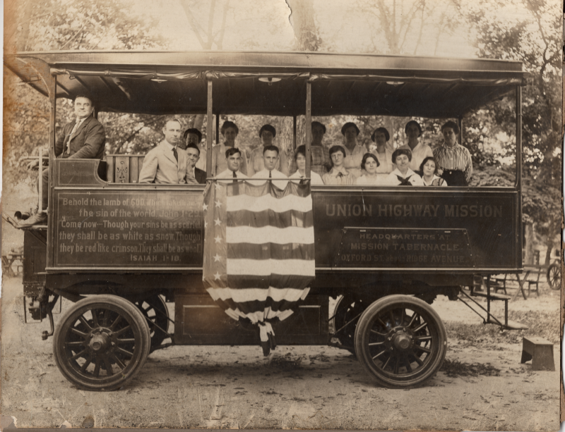Pastor E.S. Williams smiles with other congregants in the Gospel Wagon that is decorated with Isaiah 1:18, an American flag, and the church's name and address