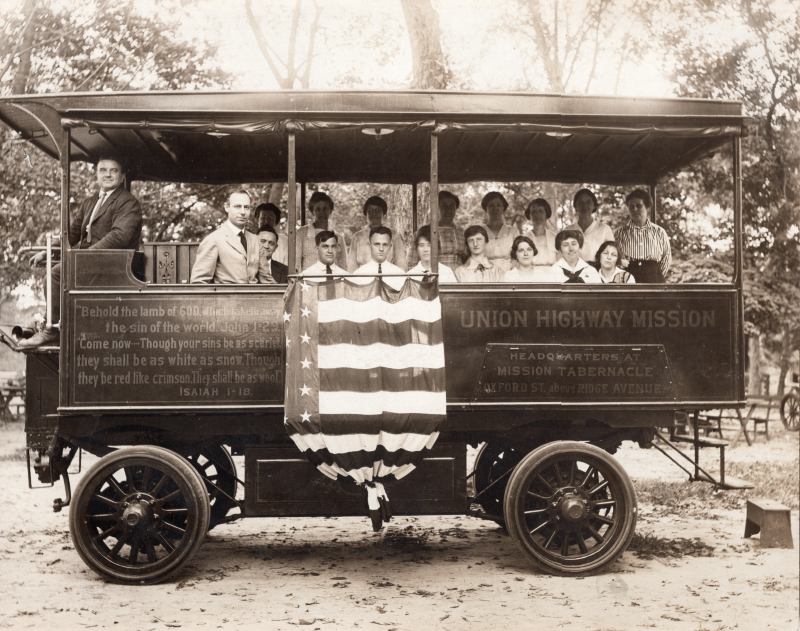 Pastor E.S. Williams smiles with other congregants in the Gospel Wagon that is decorated with Isaiah 1:18, an American flag, and the church's name and address
