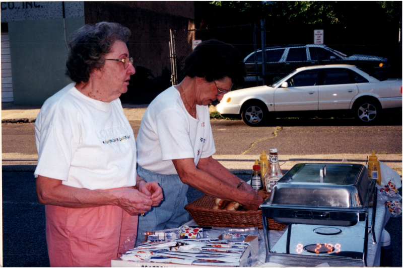 Two older women serve hotdogs