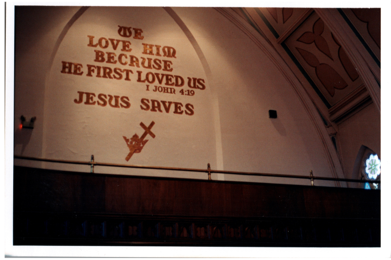 Image of the text, "We Love Him Because He First Loved Us, 1 John 4:19, Jesus Saves" with the Cross and Crown in the sanctuary of the church at 18th and Spring Garden Streets