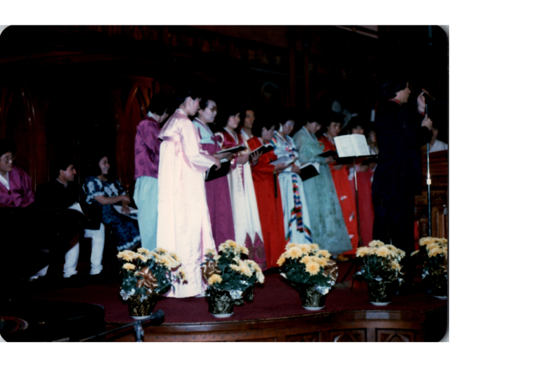A group of women in Hanbok lead a song from a hymnal on stage in the sanctuary