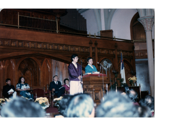 Two men in traditional Korean clothing speak from the podium