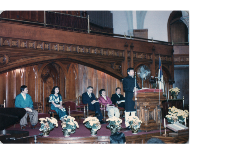 A man in traditional South Asian clothing speaks at the pulpit