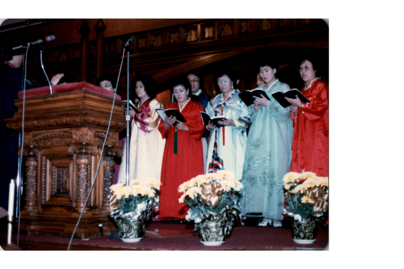 A group of women in Hanbok lead a song from a hymnal on stage in the sanctuary