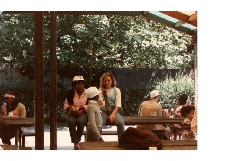 Two women talk to a young boy at picnic tables
