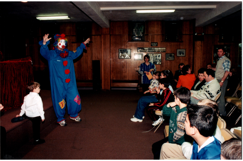 A man in a clown suit performs for a group of kids