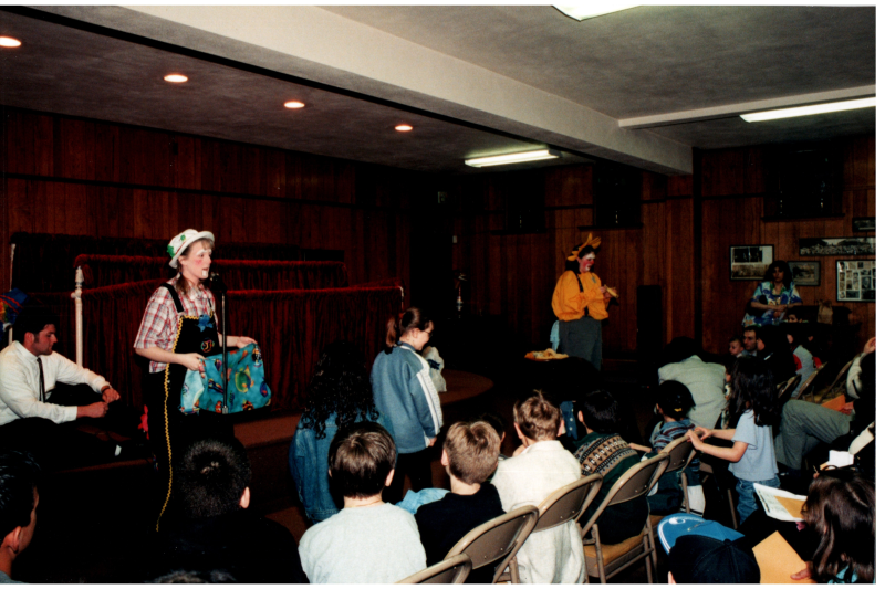 Adults in costumes adress a room of children next to a puppet stage