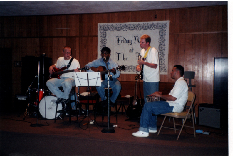 Mike Wulin, Pastor Kurruvilla, and two men perform in front of the "Friday Night at The Tab" banner