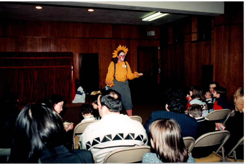 A woman in clown clothing speaks to an audience
