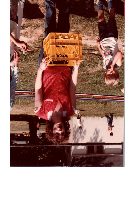 A woman holding a yellow crate organizes a game for children