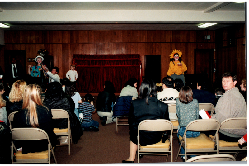 People in clown costumes address an audience of children