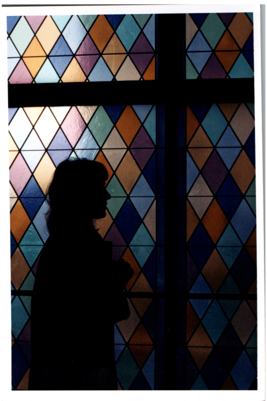 A woman stands in front of stained glass