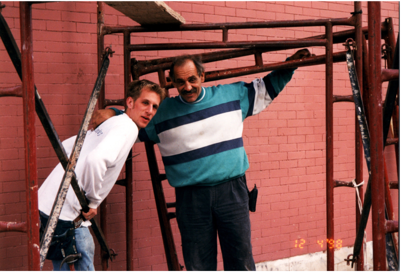 Men smile together working outside