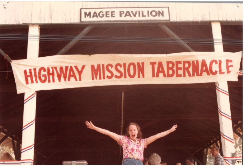 A woman poses under a "Highway Mission Tabernacle" banner