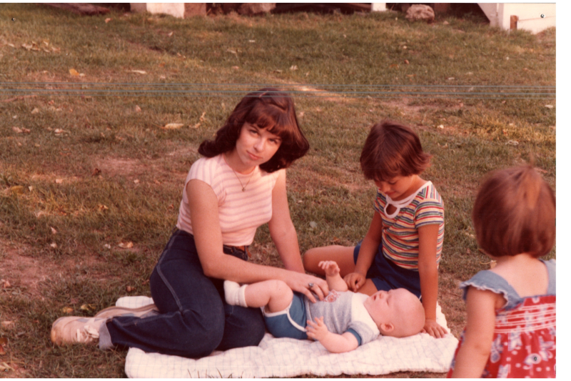 A woman sits with a girl and a baby on the grass