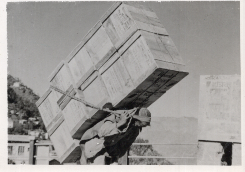 Image from the McDearmids of a man carrying five wood crates on his back using a rope
