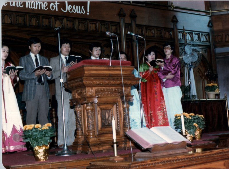 A group with several people dressed in traditional Korean clothing lead a song from hymnals