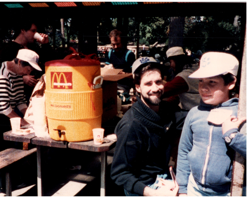A man smiles with a boy under a pavillion with refreshments