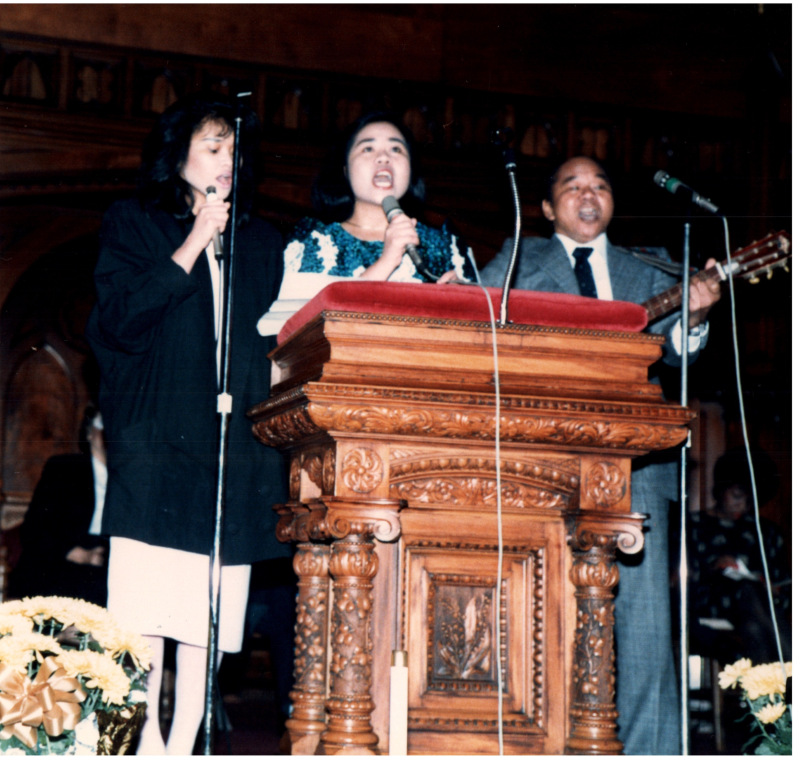 Two women and a man sing together to a guitar