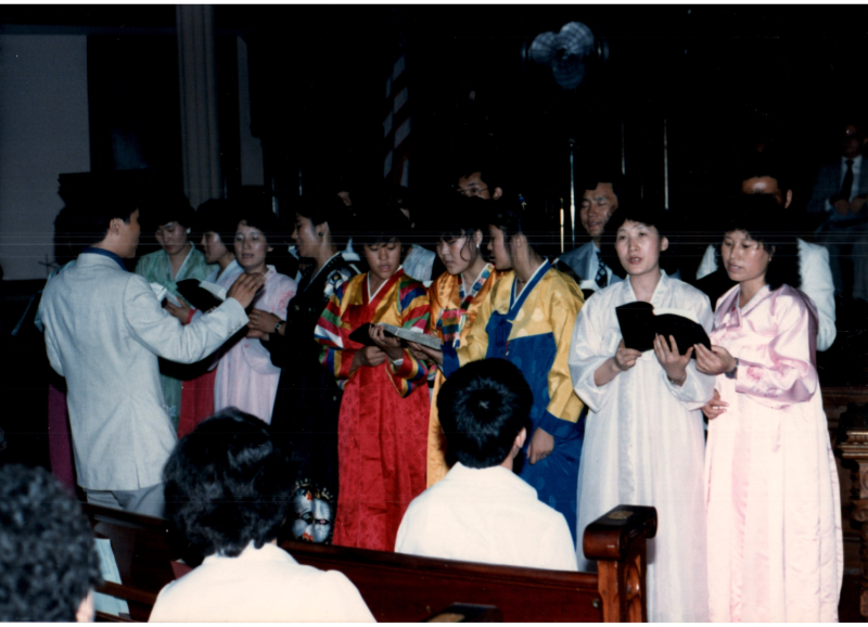 Women in hanboks lead a song from a hymnal