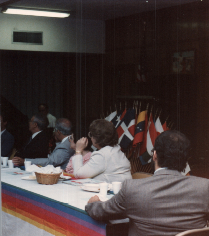 Mrs. Bogdan sits with others around a table with international flags in the background