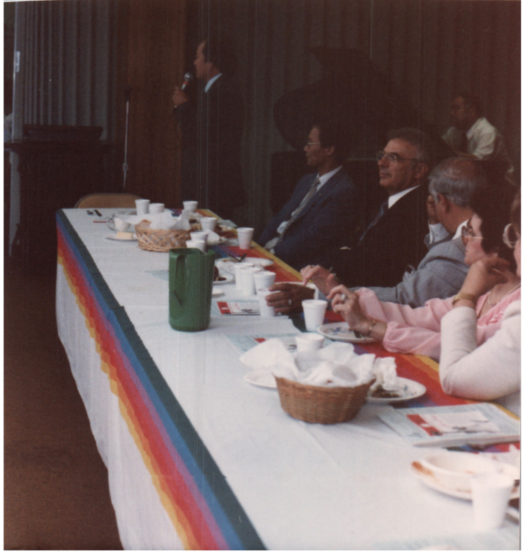 Rev. Bogdan sits with others around a table with international flags in the background