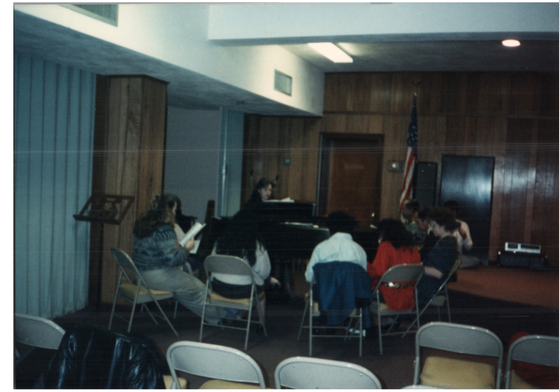 A group sings around a piano