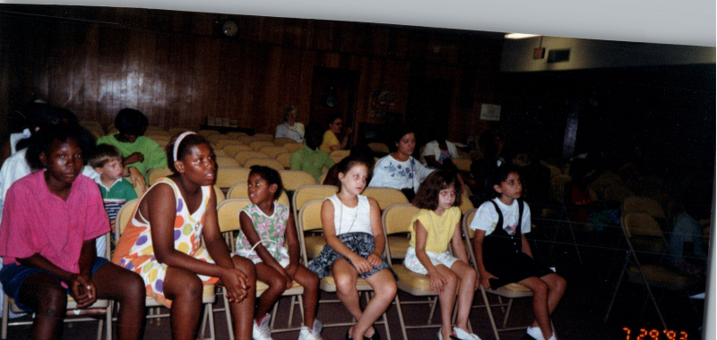 Children face Mrs. Abe Oliver on a stage