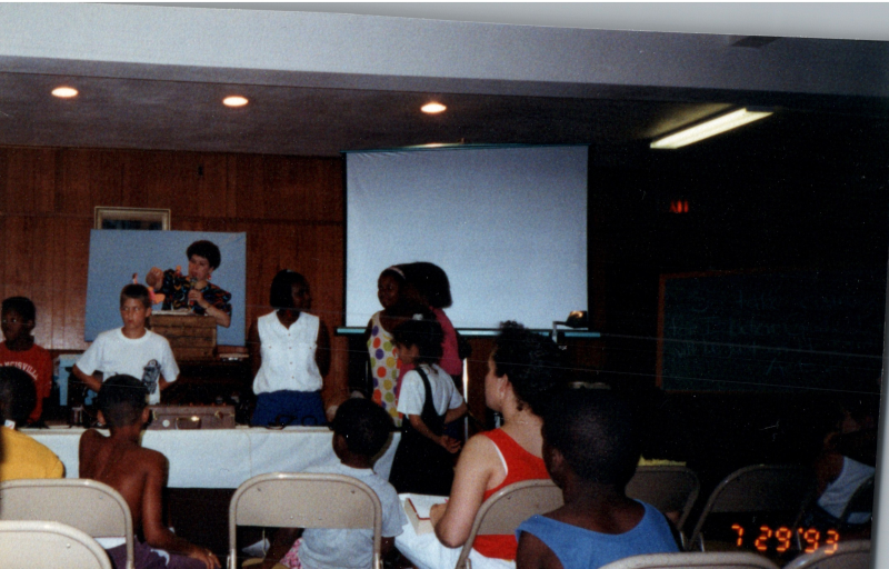 Children face Mrs. Abe Oliver on a stage