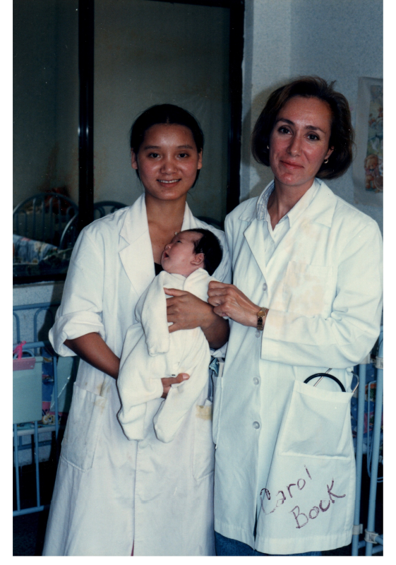 Carol Bock stands with another woman in a doctor's coat with a baby
