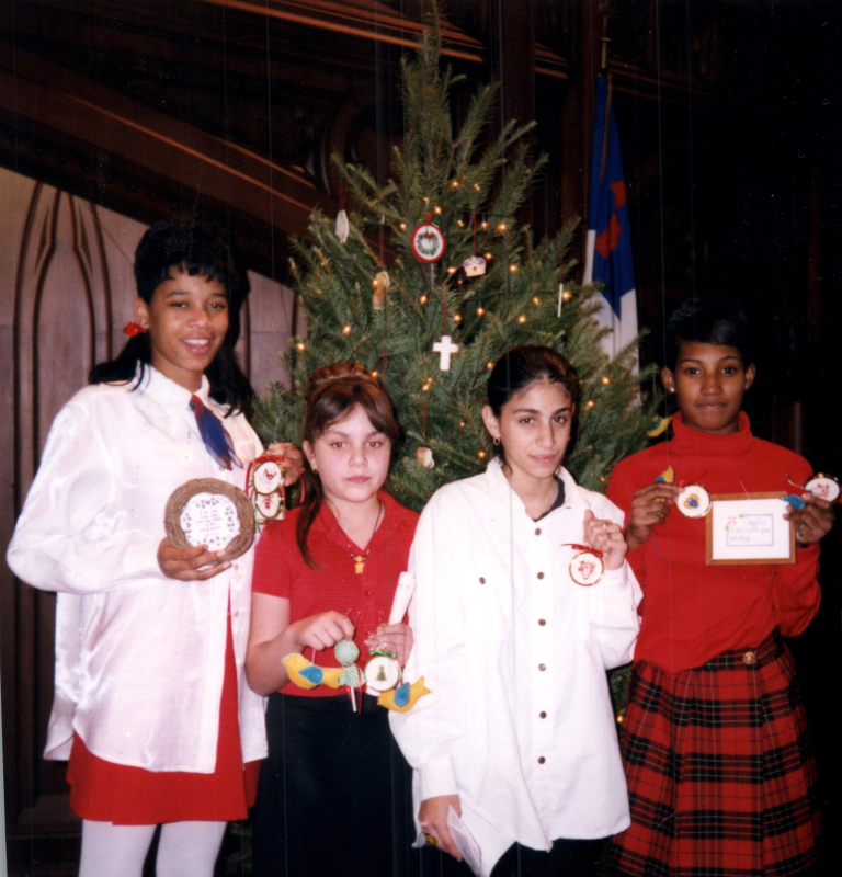 A group of girls hold up crafts in front of a Christmas tree
