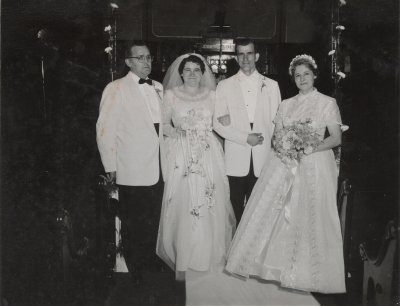 A bride and groom stand with a woman holding flowers and a man