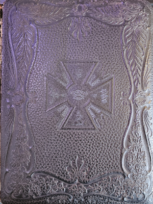 Black leather-bound cover with imagery of a skull and crossbones, an eye with three rings, hands shaking, an other imagery 